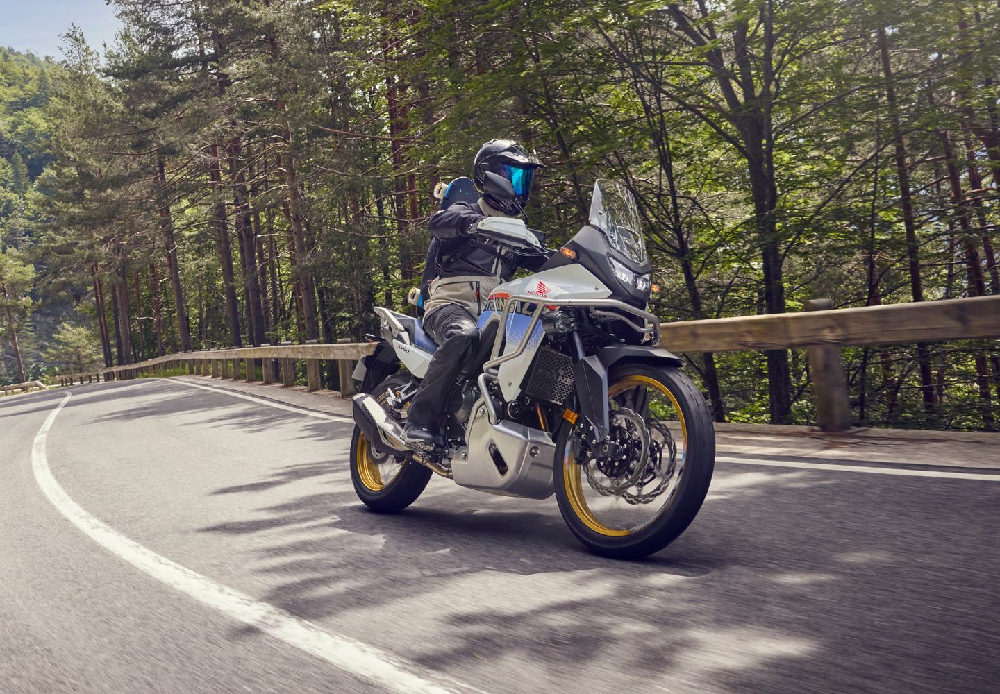 Motorcyclist riding a white sport bike on a curving forest road with guardrail