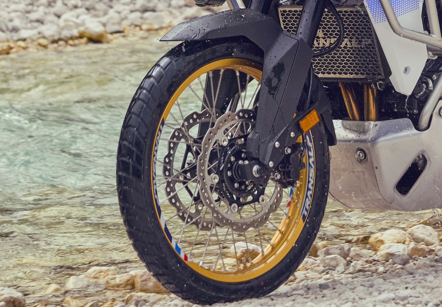 Front wheel of a black motorcycle with gold rim on a rocky road, close-up view