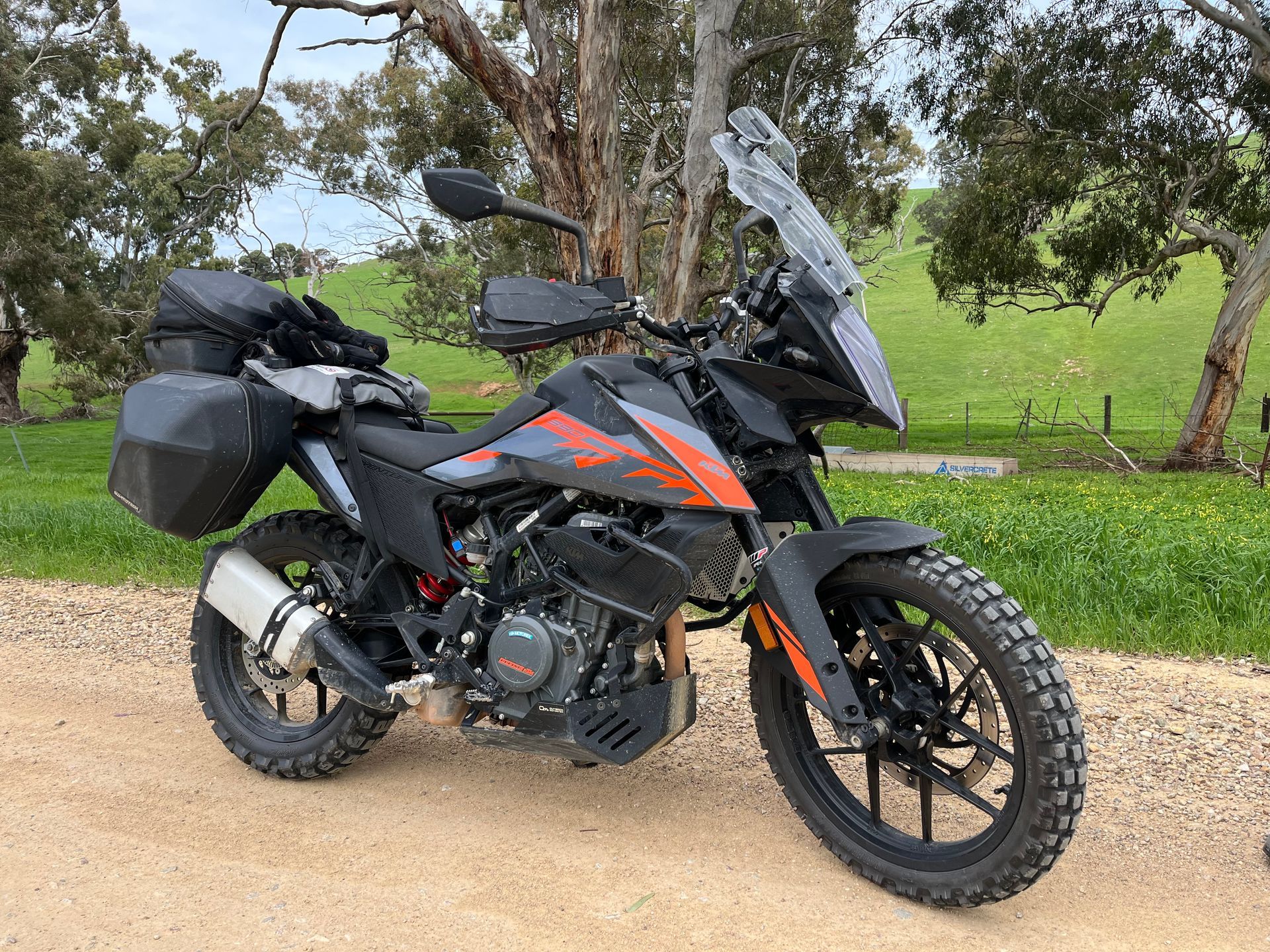 Black adventure motorcycle with saddlebags parked on a dirt road by trees and green grass
