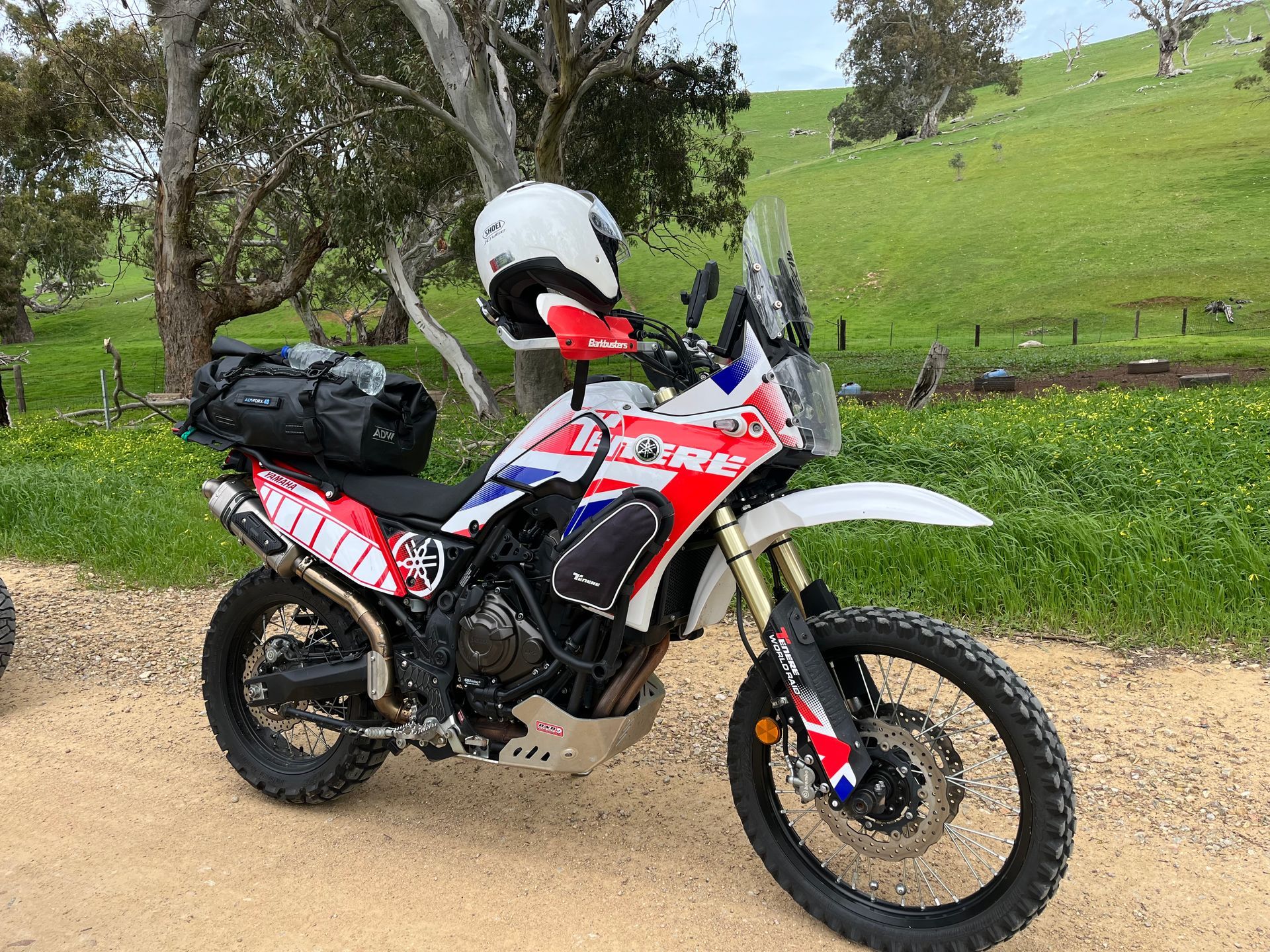 Red, white, and black adventure motorcycle parked on a dirt path in a grassy rural area.