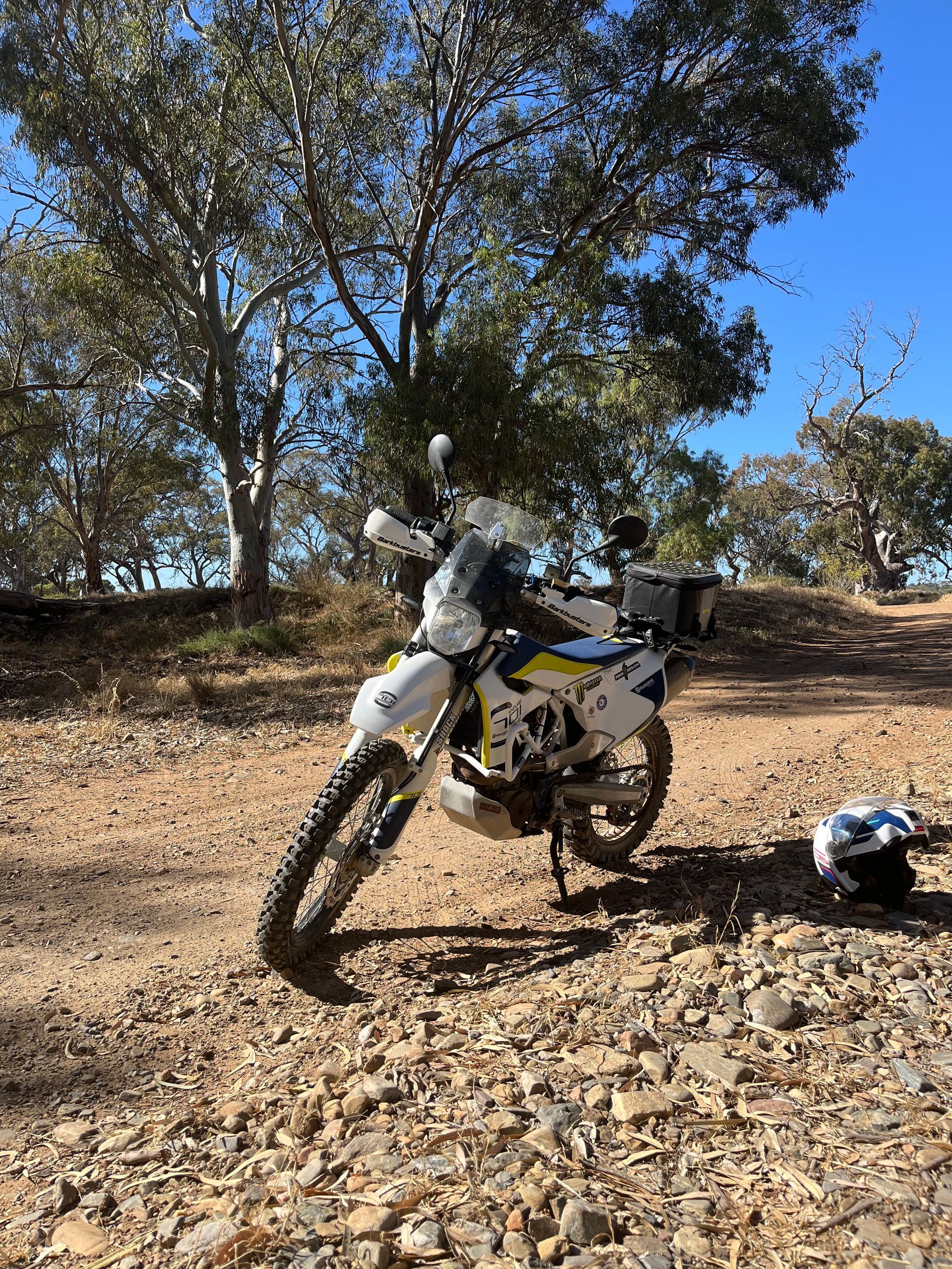 Dirt bike parked on a rocky trail under trees on a clear day