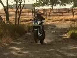 Motorcyclist riding on a dirt path beside a wooden fence in a rural field