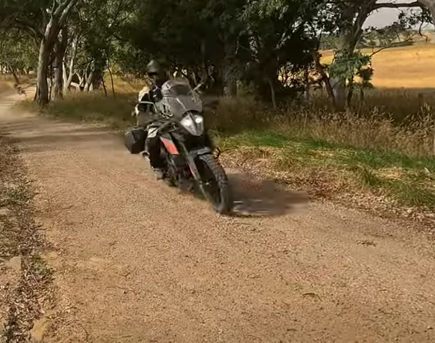 Motorcyclist riding on a dusty dirt road lined with trees