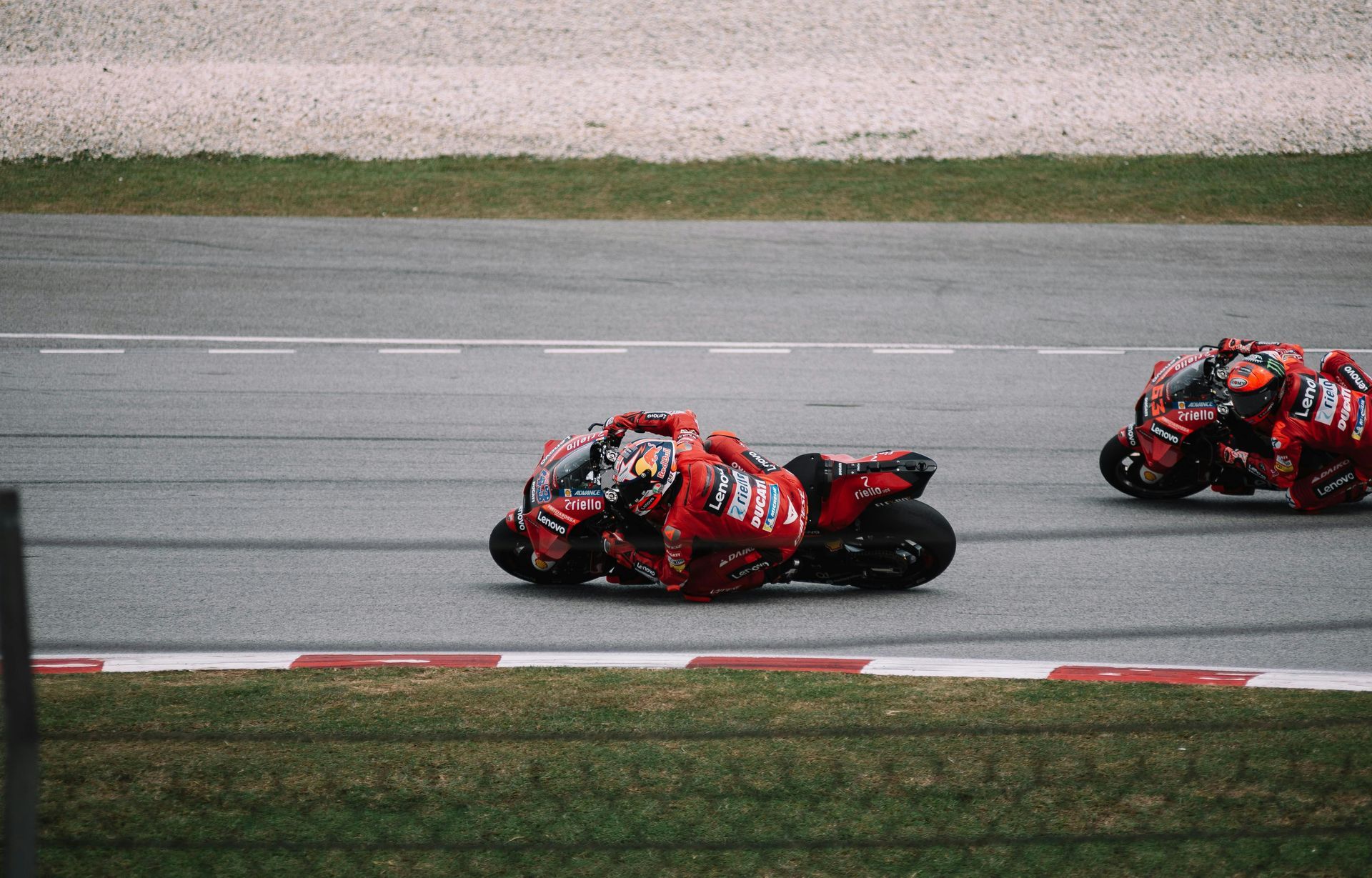 Two red race motorcycles leaning into a turn on a track, one leading the other.