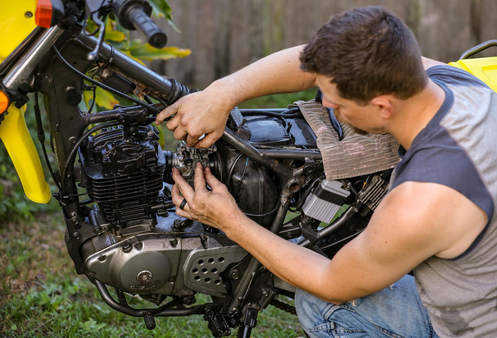 Man working on a motorcycle engine outdoors, tightening parts by hand