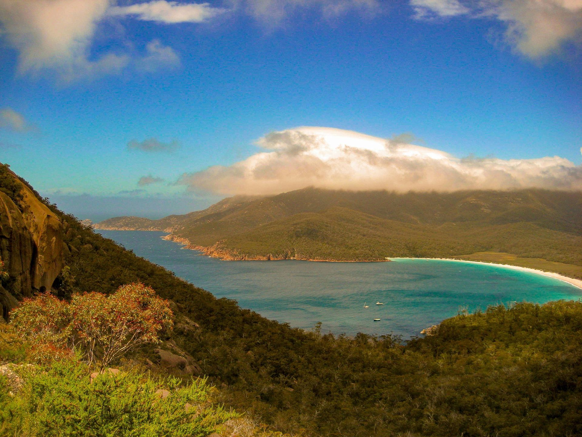 Tropical bay with turquoise water, green mountains, and a cloudy sky under bright sun