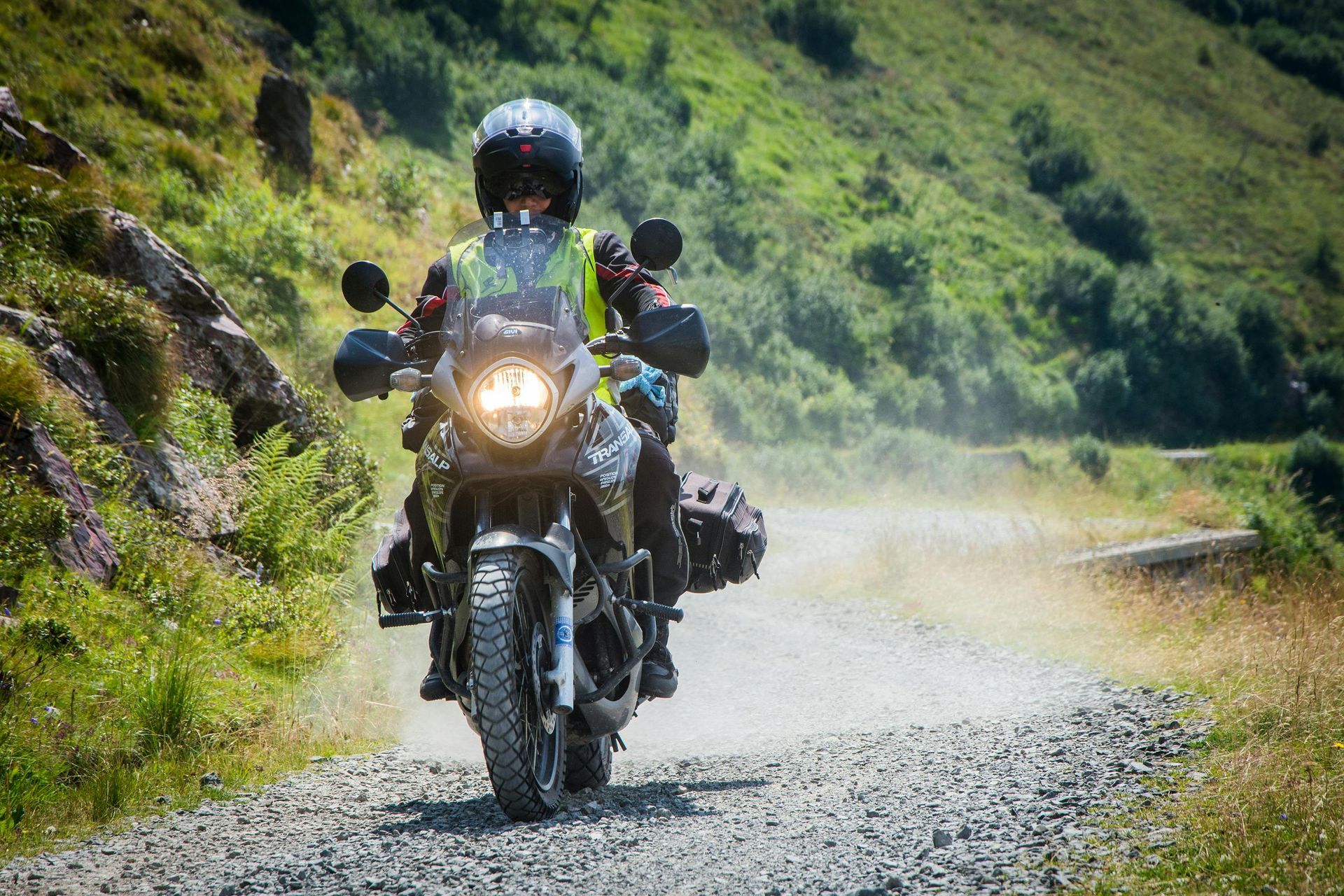 Motorcyclist rides on a gravel road through green hills, kicking up dust
