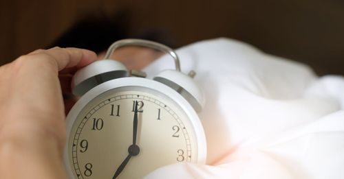 A person is holding an alarm clock in their hand while laying in bed.