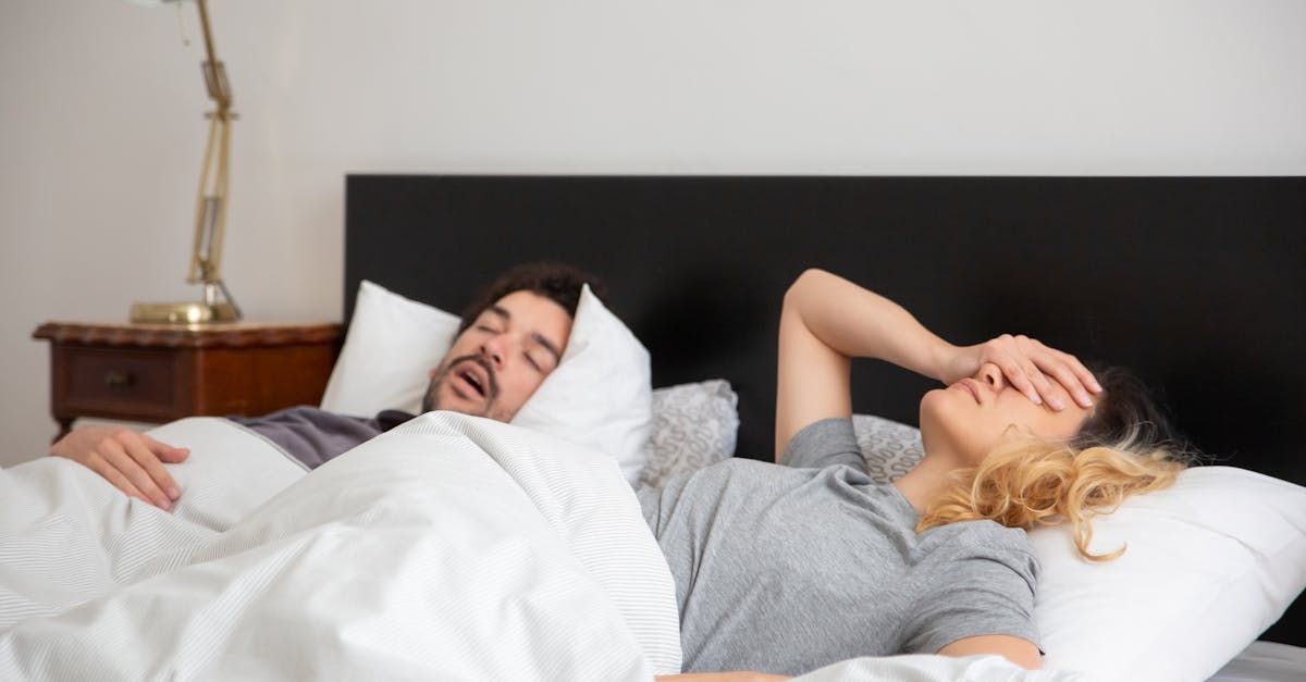 A man and a woman are sleeping in a bed . the woman is covering her face with her hand.