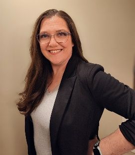Woman wearing glasses, a blue patterned top, smiling at the camera, against a white backdrop.