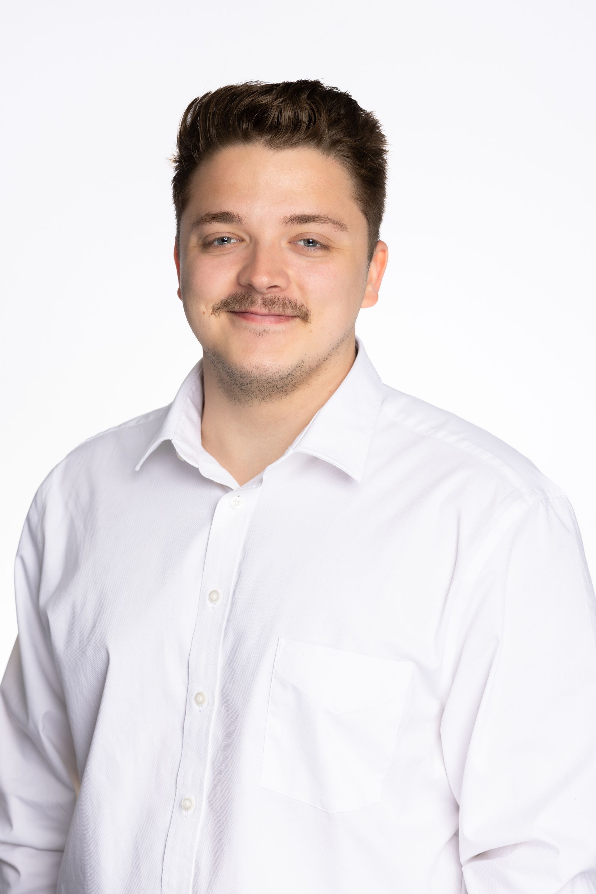 Man in white shirt smiling at the camera against a white background. He has a mustache.