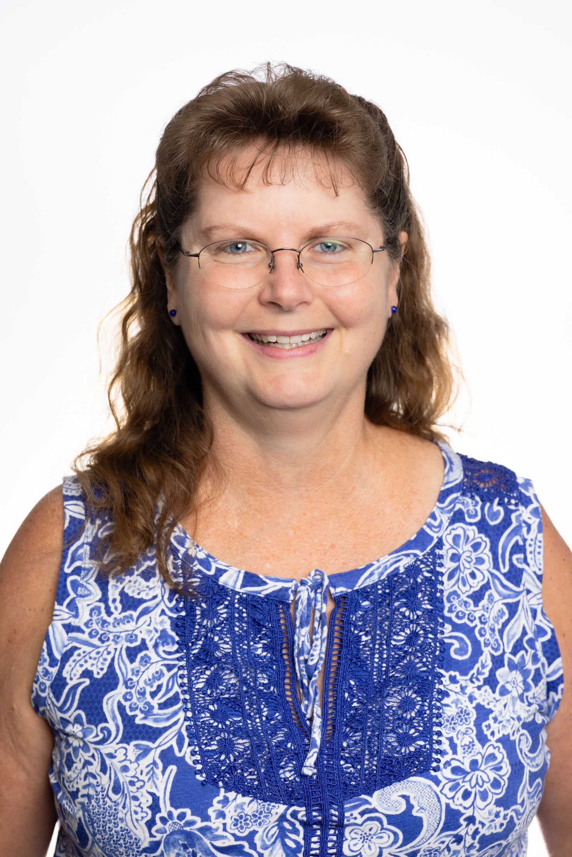 Woman with glasses, smiling, wearing a blue and white patterned sleeveless top, in front of a white background.
