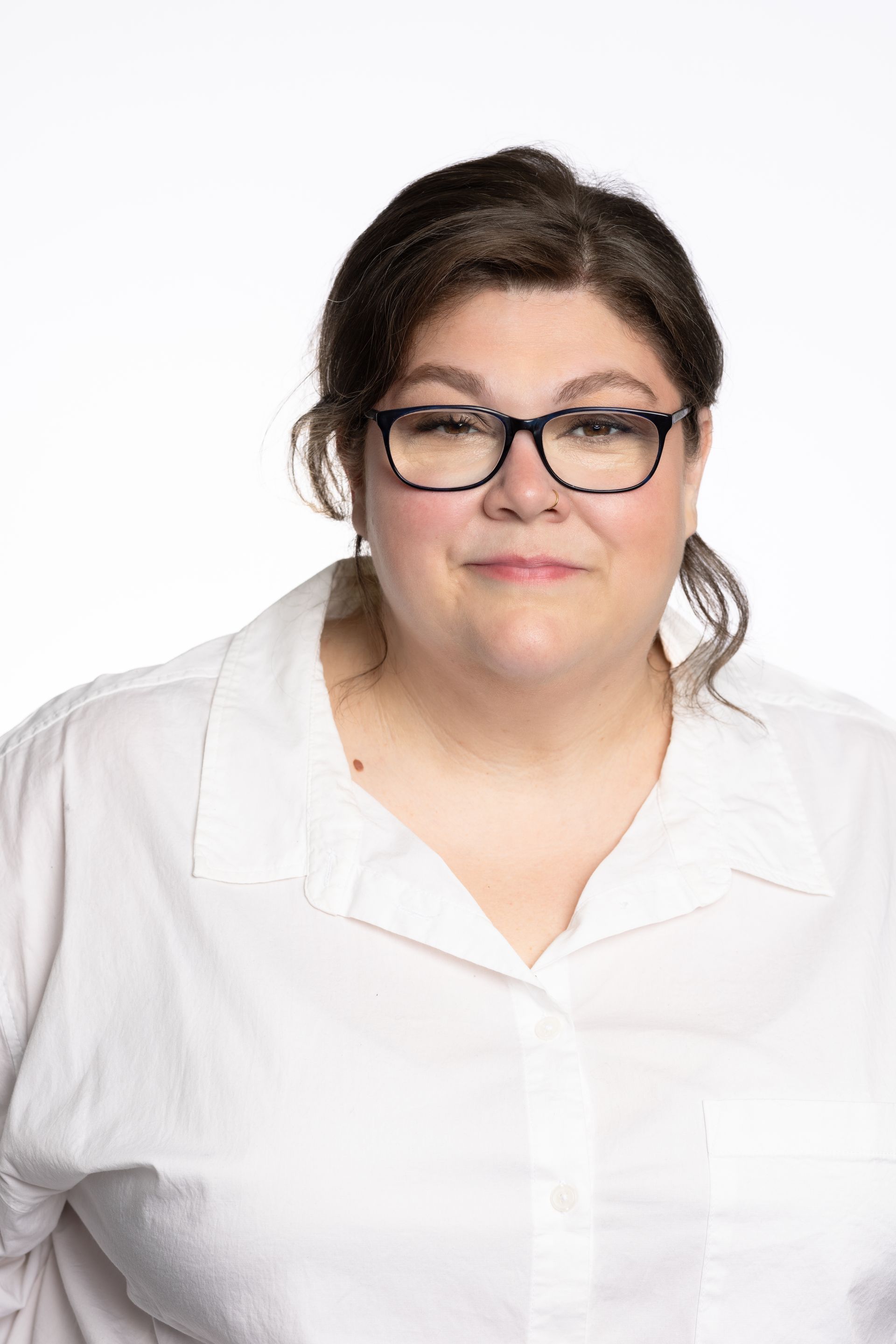 Woman with glasses smiles, wearing a white button-down shirt, set against a white backdrop.