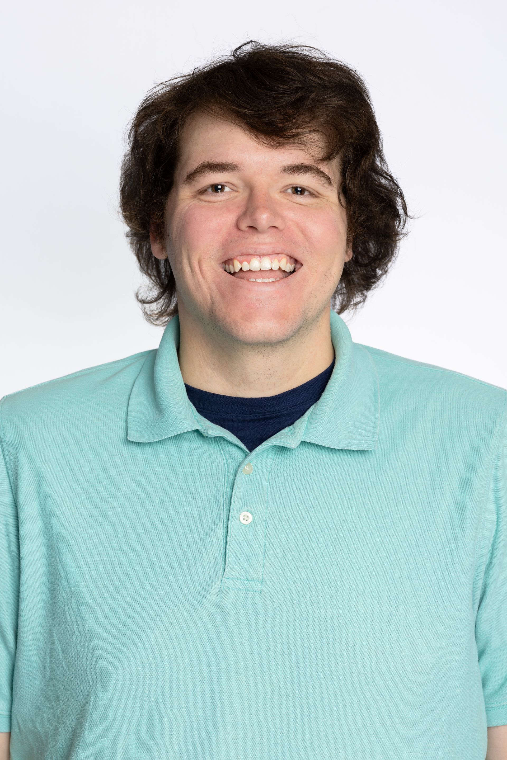 Smiling person with dark curly hair wearing a blue polo shirt.