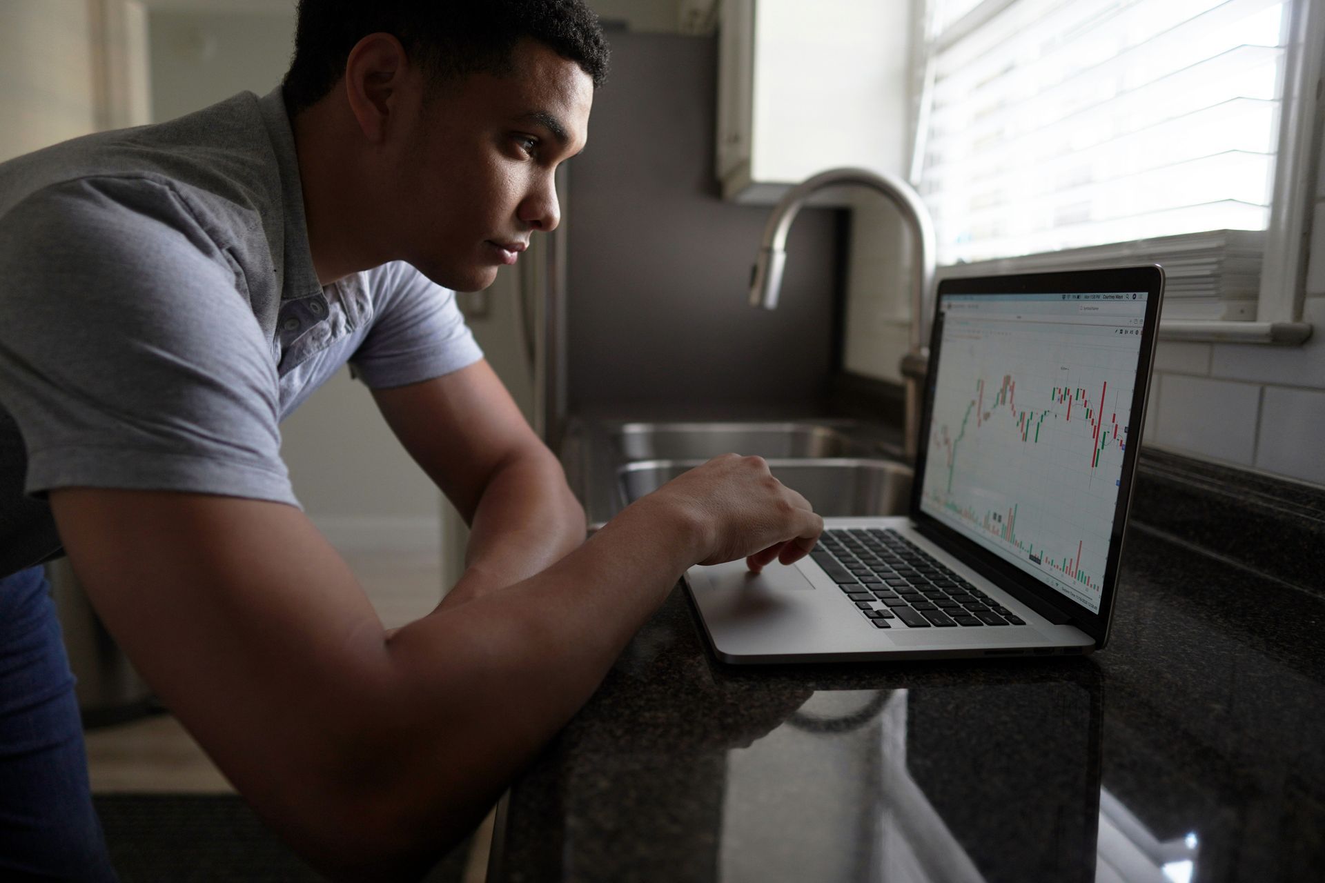 Man in a kitchen looking at a laptop, with charts displayed on the screen.