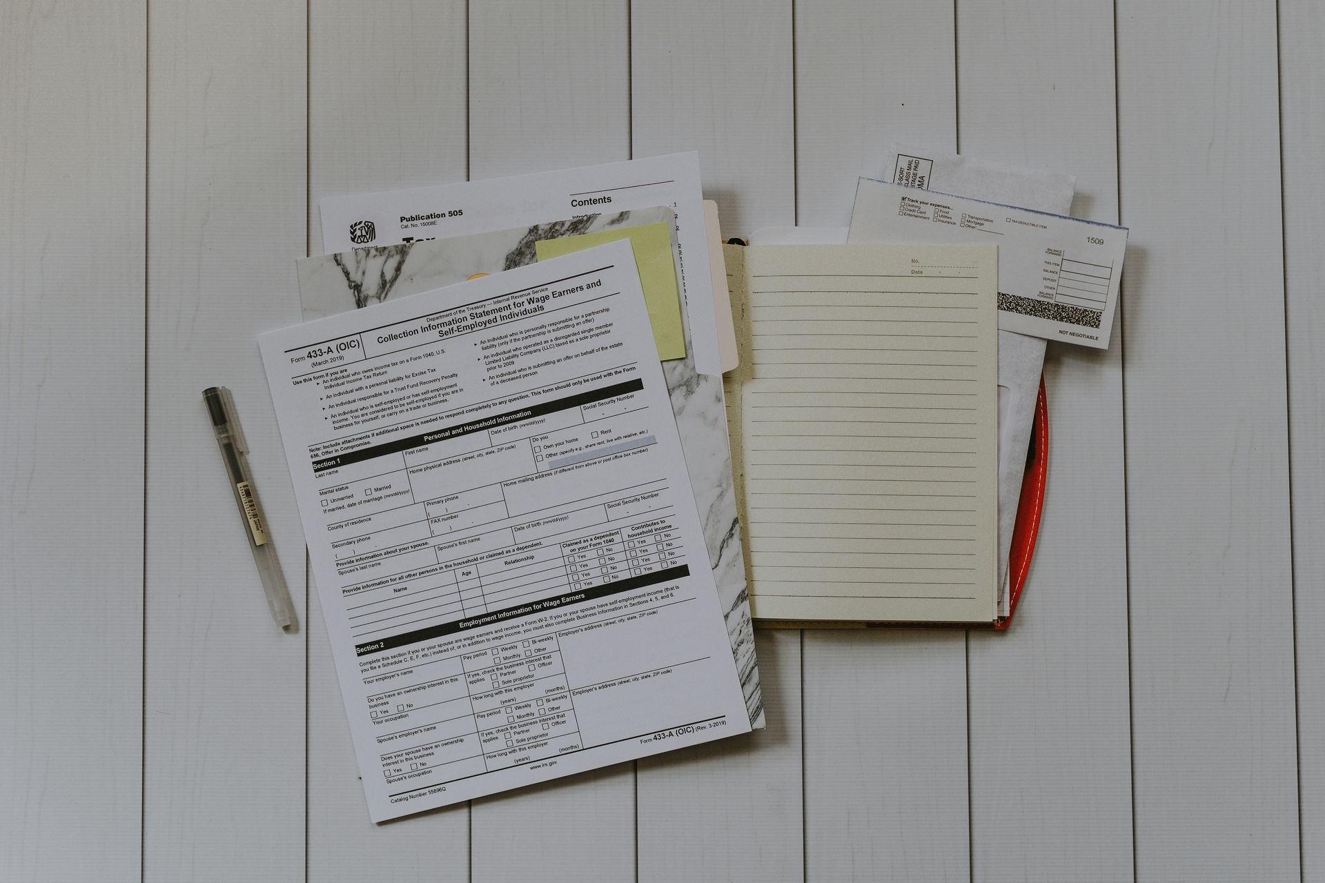 Pile of papers and receipts with a pen, on a white wooden surface.