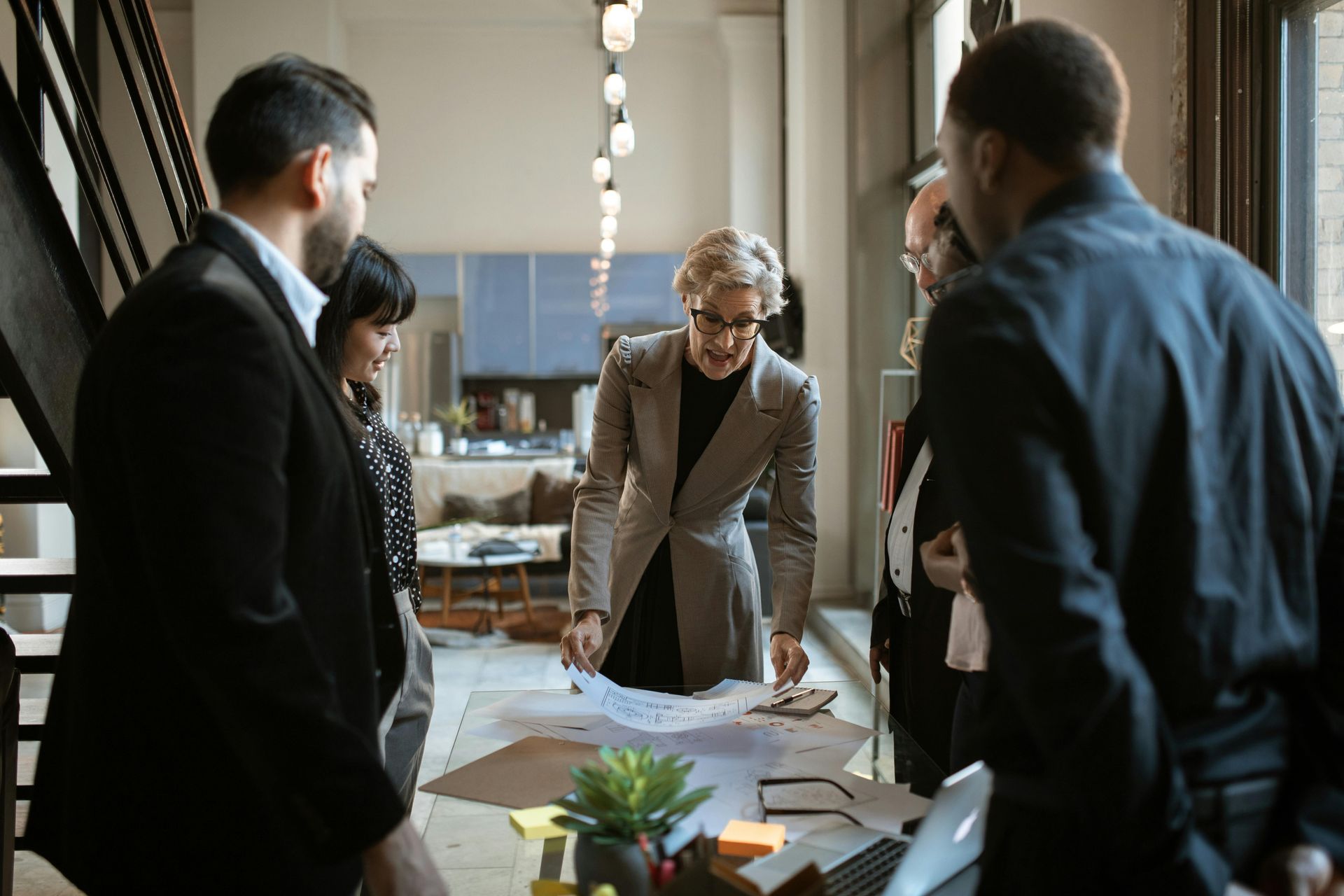 Group of people in business attire around a table, looking at blueprints. Interior office setting.