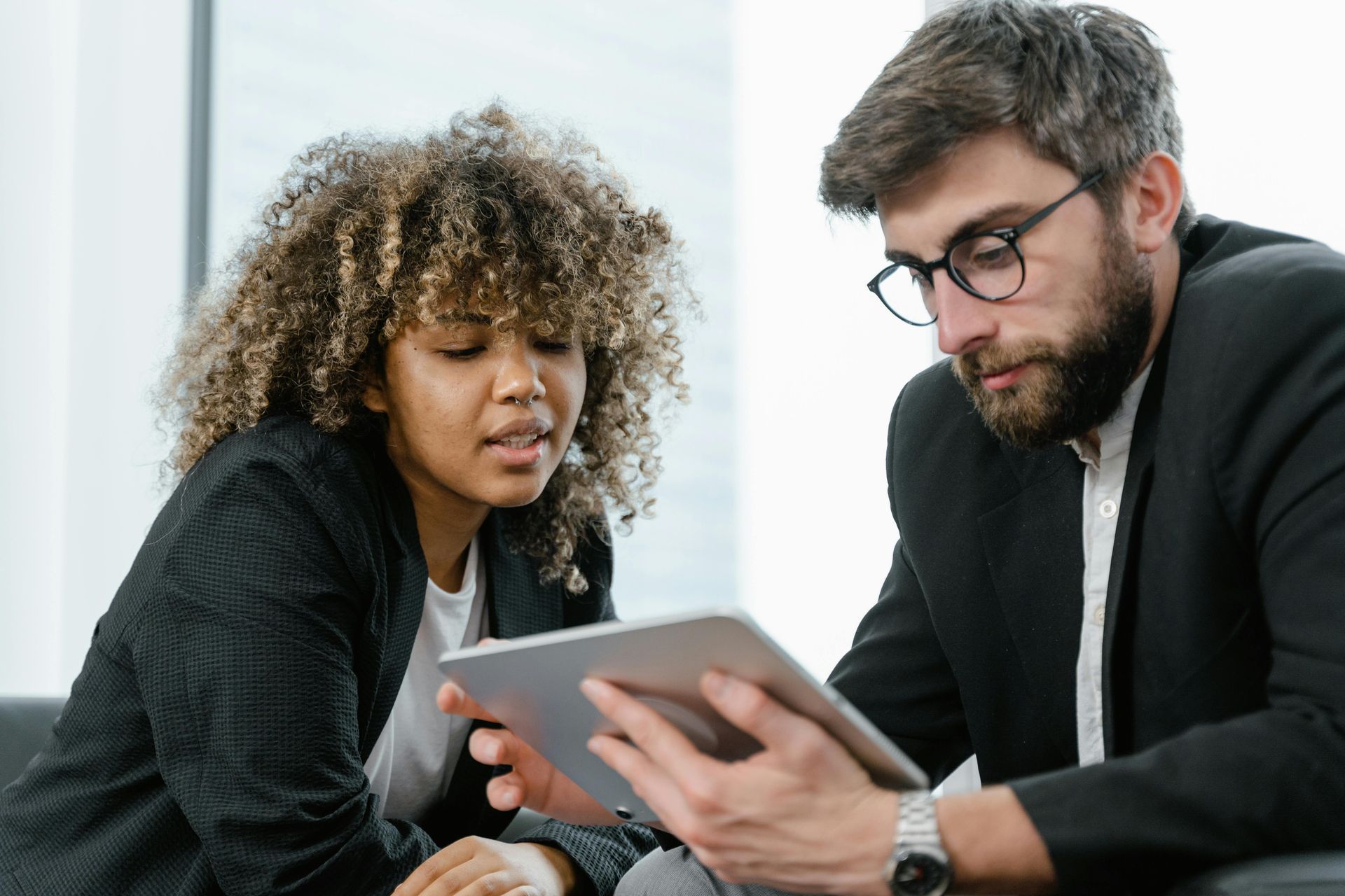 Woman and man in suits reviewing a tablet, indoor setting.