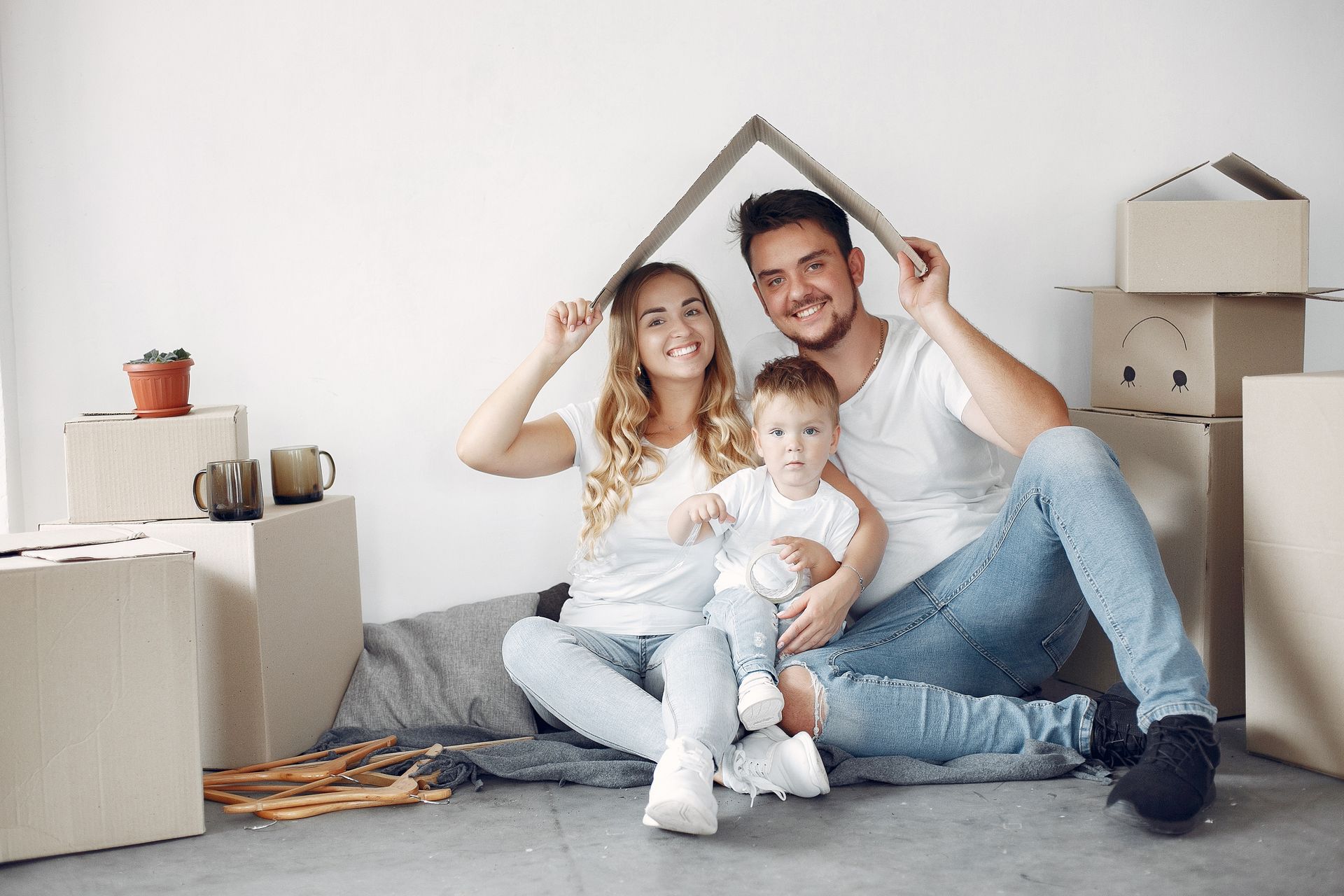 Una familia está sentada en el suelo en su nuevo hogar sosteniendo una casa de cartón. | Fonrecar. Organizadores de eventos