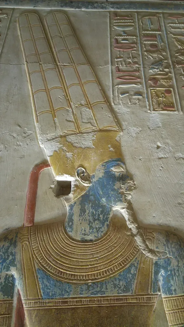 Ancient painted relief of a pharaoh’s head and headdress on a temple wall, with hieroglyphs beside it