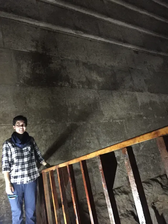Person standing on a slanted stairwell beside a railing in a dim concrete interior