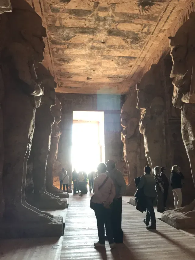 People walking through a carved stone temple hall toward a bright doorway