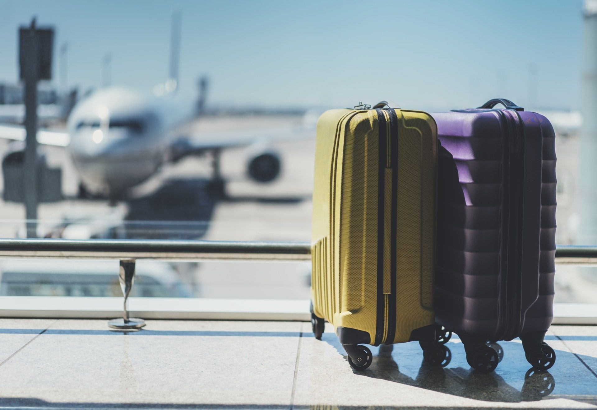 Two suitcases by an airport window, with a blurred airplane in the background.
