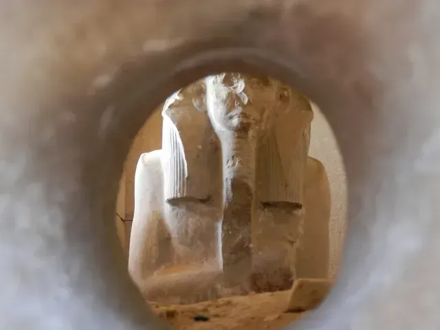 Sandstone Buddha statue viewed through a circular opening in a cave-like wall