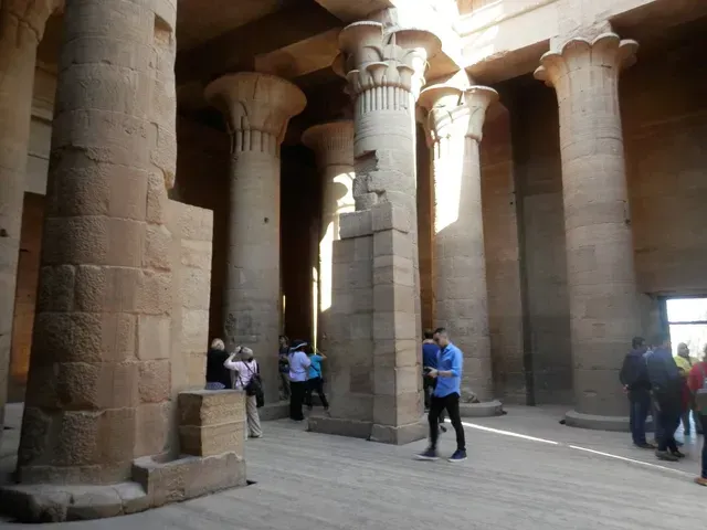 People touring an ancient stone temple with tall columns and carved pillars.