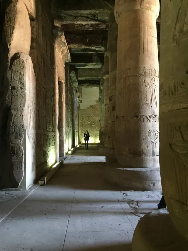 Ancient temple corridor with tall stone columns and a lone person walking in the distance
