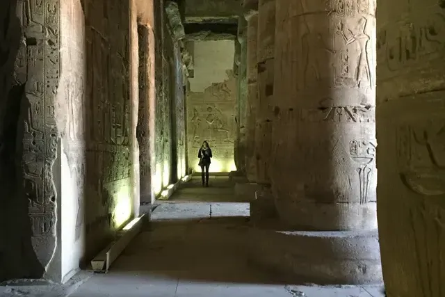 Ancient stone temple corridor with carved columns and a lone person standing in the distance
