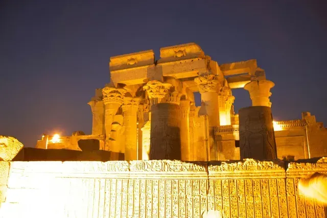 Illuminated ancient stone temple ruins at night with engraved foreground wall