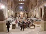 Grand hallway in a museum with visitors walking beneath ornate arches and sculptures