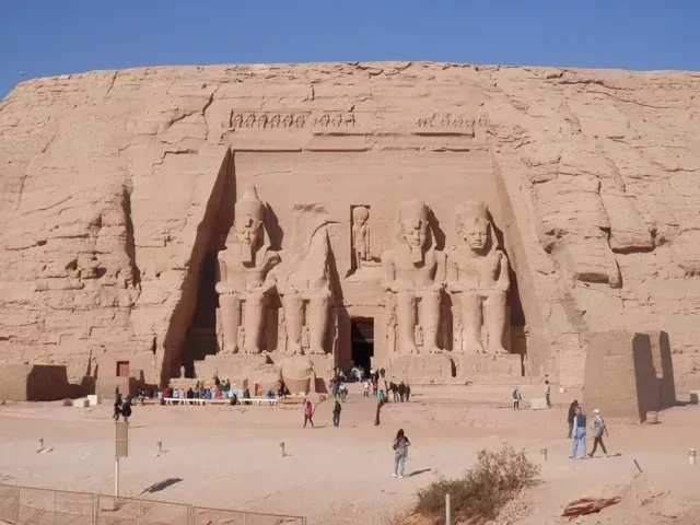 Ancient rock-cut temple facade carved into a desert cliff, with visitors gathered below