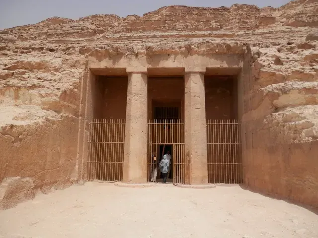 Rock-cut desert tomb entrance with metal gates and a person standing in the center opening
