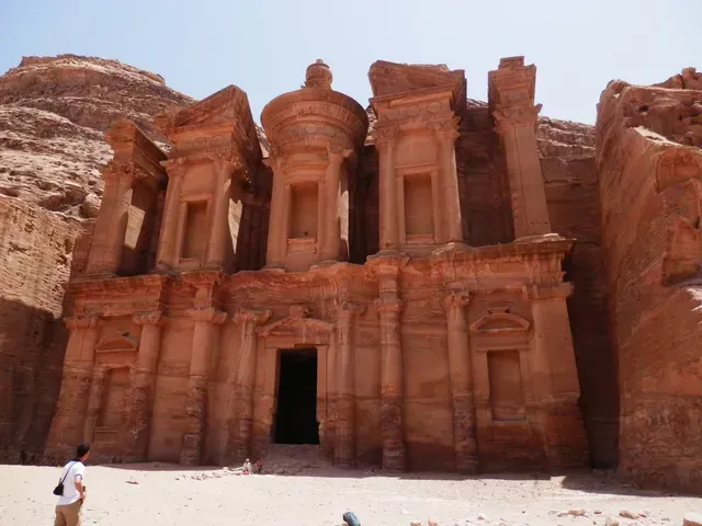 Ancient red sandstone rock-cut temple facade in a desert landscape with a person standing nearby