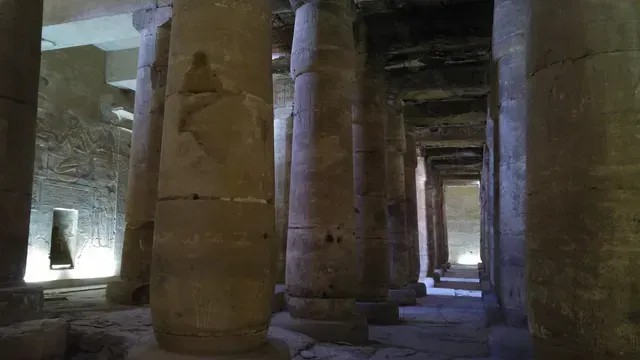 Ancient stone temple interior with massive columns and a lit passageway in the distance