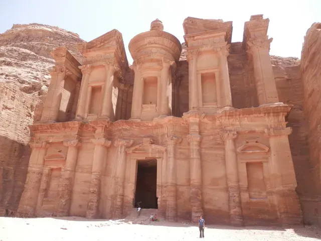 Ancient sandstone temple facade carved into a rocky cliff, with a small person standing in front.