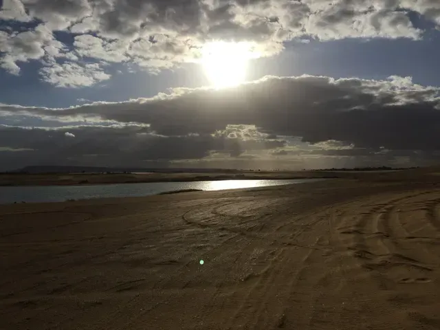 Sunlit sandy beach with dark clouds over the water and tire tracks in the foreground