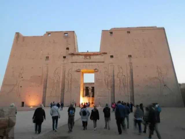 Tourists walking toward a massive stone temple gate at dusk, lit by warm lights