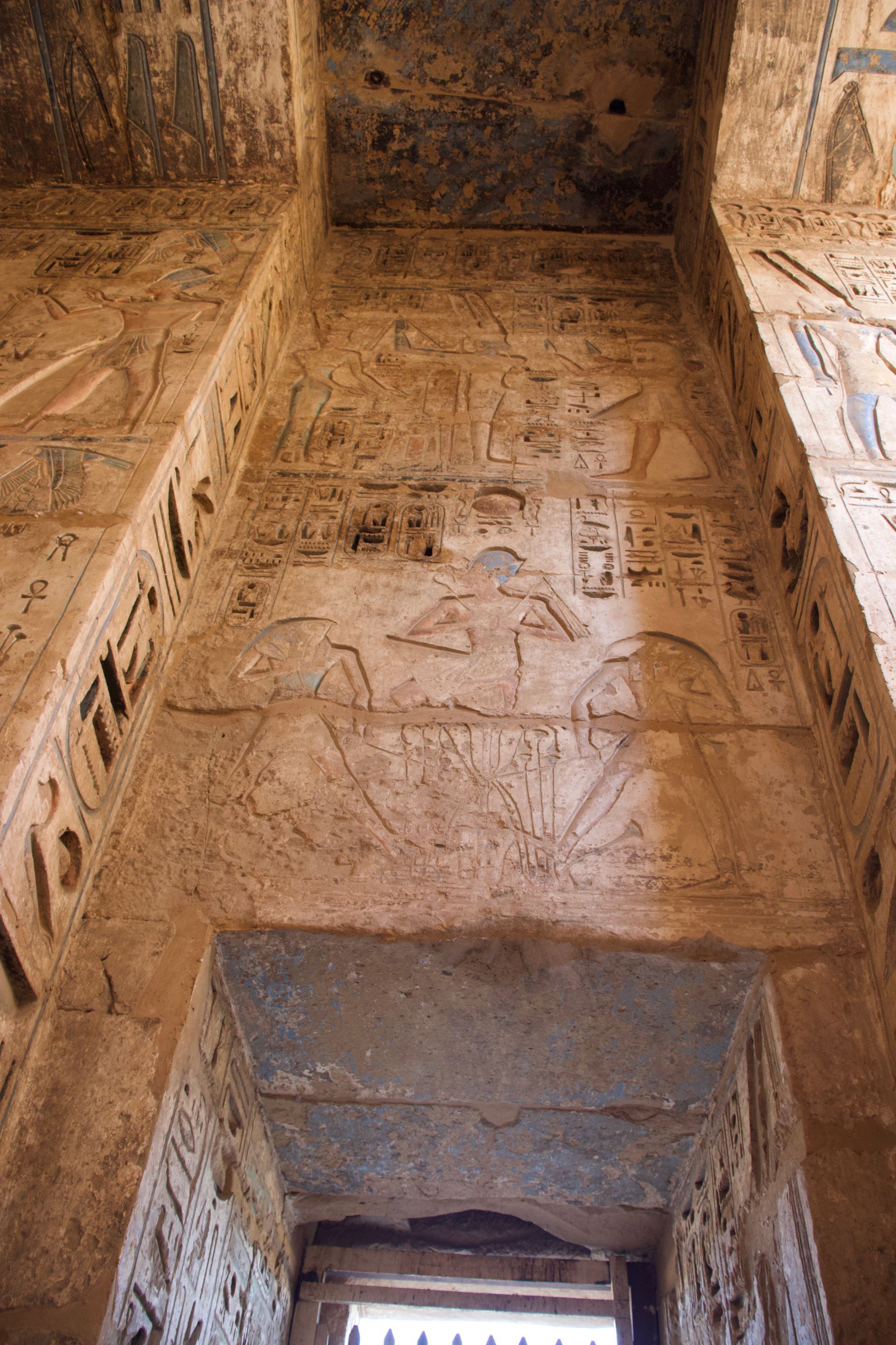 Ancient sandstone wall with carved reliefs and a doorway at the bottom