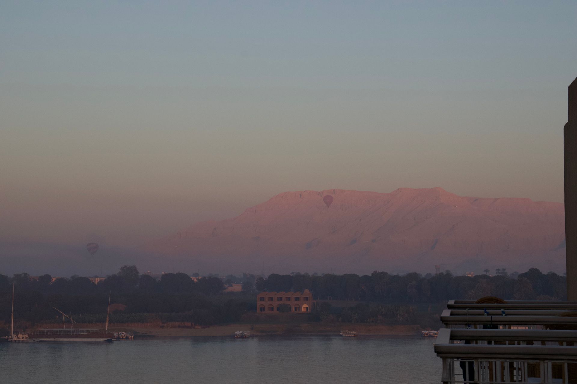 Calm waterfront at dusk with a pink-lit mountain and silhouetted shoreline buildings