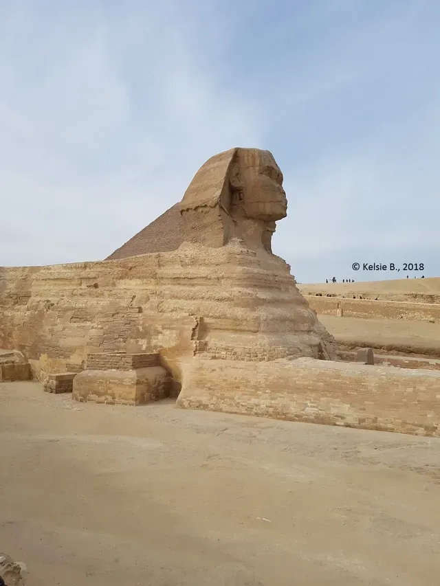 Weathered Great Sphinx of Giza in a sandy desert under a pale blue sky.