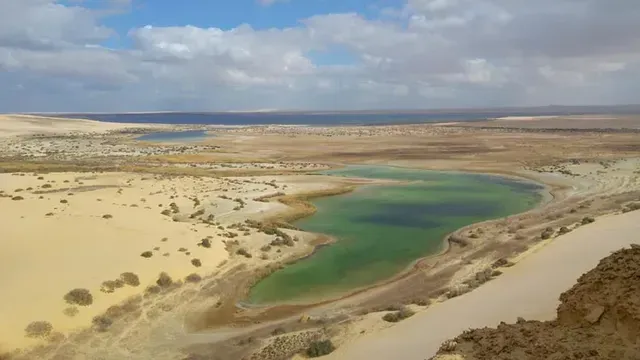Aerial view of a desert landscape with a turquoise lake and sandy shore under cloudy skies