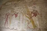 Ancient wall painting of several figures in robes holding staffs and objects, in faded earth tones