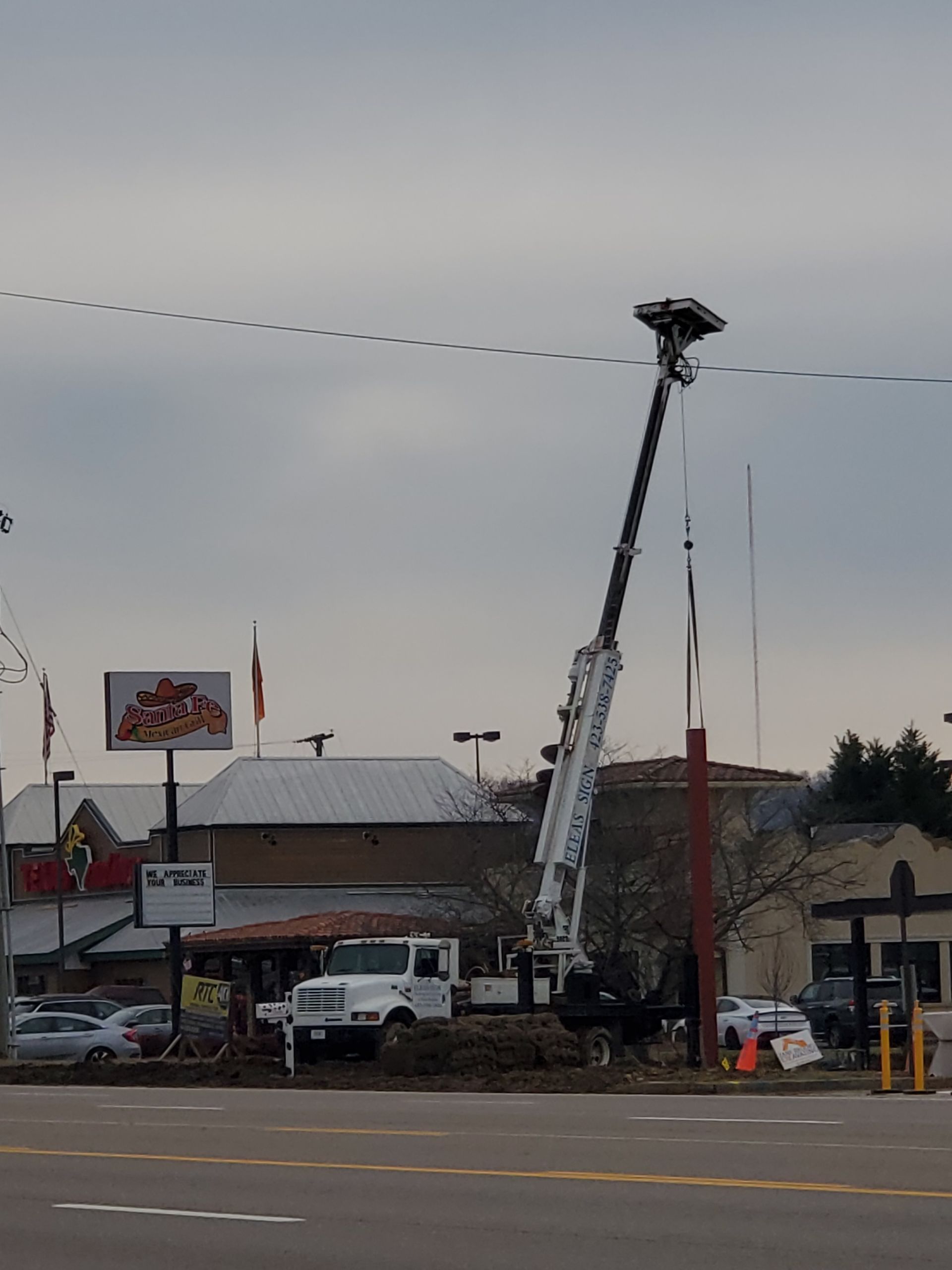 A crane is lifting a light pole in front of a burger king restaurant