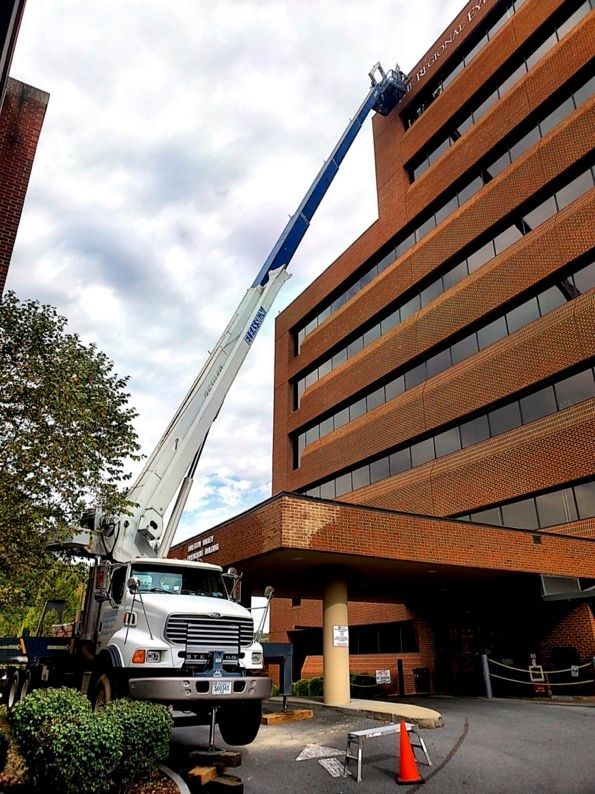 A white truck with a crane attached to it is parked in front of a large brick building