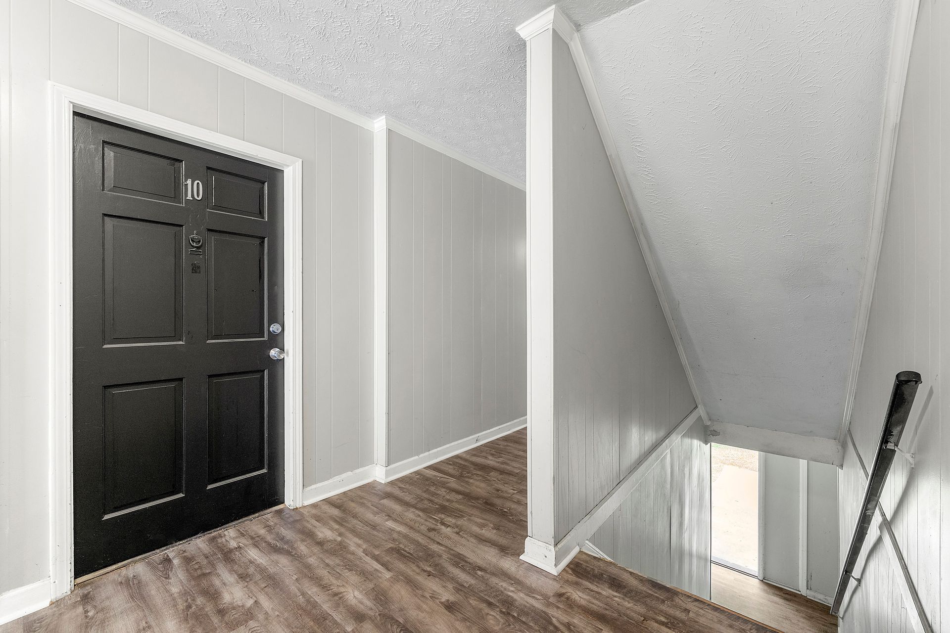 Stair landing with black front door, gray walls, wood floor, and staircase railing on the right