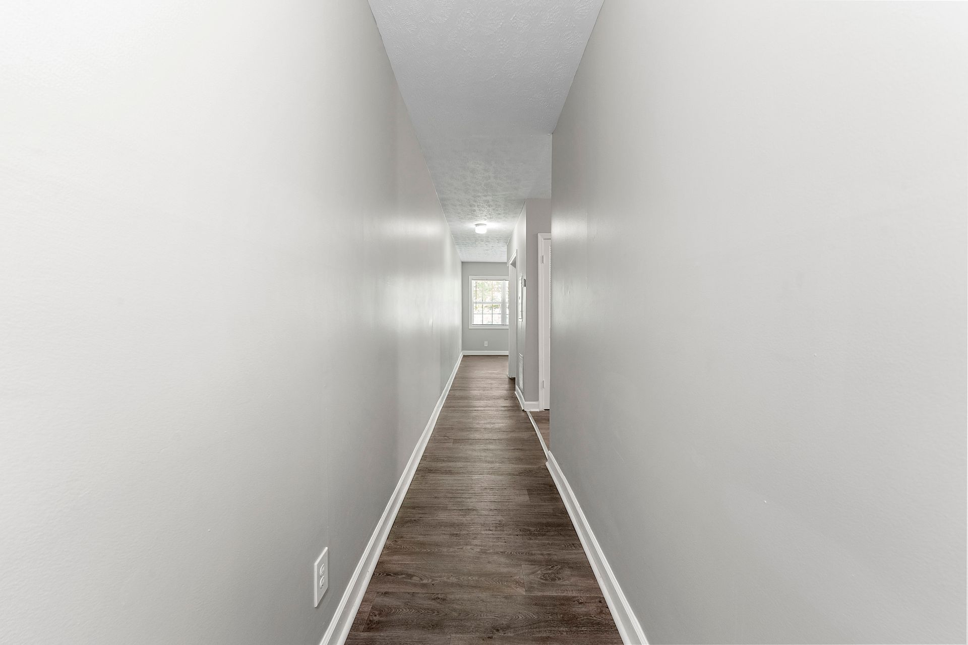 Narrow white hallway with gray carpet leading to a bright doorway at the far end