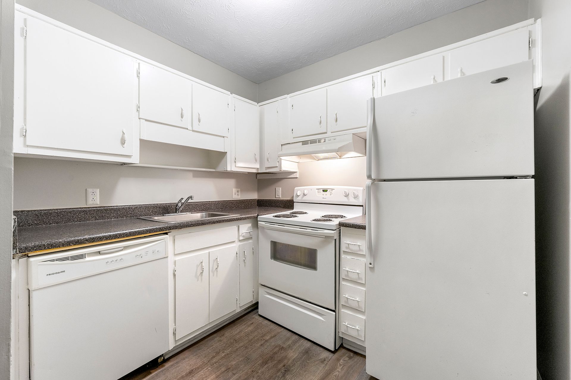 Small white kitchen with cabinets, stove, refrigerator, and granite countertops